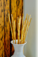 Bundle of natural dried river cane bamboo sticks in white ceramic vase against wood panel background.