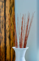 A vase with preserved branches of Asian Willow with a burnt oak color, placed against a wooden backdrop.