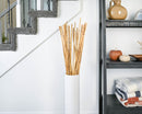 Dried natural river cane bamboo sticks in bulk, arranged in a tall white vase near staircase and shelf.