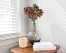 Burgundy dried hydrangea stems in clear glass vase on wooden table with natural light shadows.