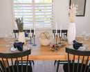 Natural dried white starflower bunches displayed in bulk on a dining table with modern black chairs and tableware.