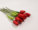 A bundle of red artificial tulips with green leaves, tied together at the stems with a ribbon.