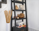Black ladder shelf displaying folded blankets, dried floral decor, and pottery in natural tones.
