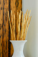 Natural dried river cane bamboo sticks in bulk arranged in white ceramic vase against wood background.