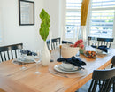 Dried natural green spear palm frond in white vase on wooden dining table with place settings and decor.