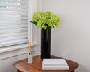 Lime green dried hydrangea spray with natural texture in tall black vase on wooden table.