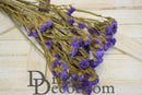 Bulk bundle of natural dried lavender statice sinuata flowers with slender stems on wooden surface.
