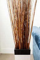 Bulk dried natural Asian willow branches in honey color arranged in a black square vase.