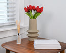 Bundle of 10-inch red tulips with green stems in beige textured vase on wooden table, dried natural bulk wholesale.