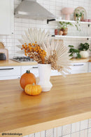 Bulk dried natural floral button flowers in warm tones arranged in white vase on wood countertop.