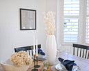 Bulk dried bleached blond bunny tails grass in tall white vase on dining table with natural decor.