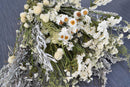 A dried white garden flower bouquet consisting of various white flowers and green foliage, arranged artistically.